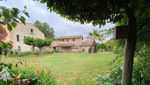 A rustic stone building with a well-maintained lawn and tropical plants. - Mas Des Fleurs - Heated pool - Child friendly gardens - Beach 10mins   (Perpignan)