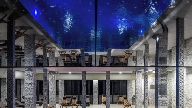 A large indoor swimming pool with a blue tint, surrounded by columns and lounge chairs. - Alexander Resort (Belgrade)