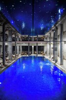 Una amplia piscina interior con un tono azul, rodeada de columnas y sillones de descanso.