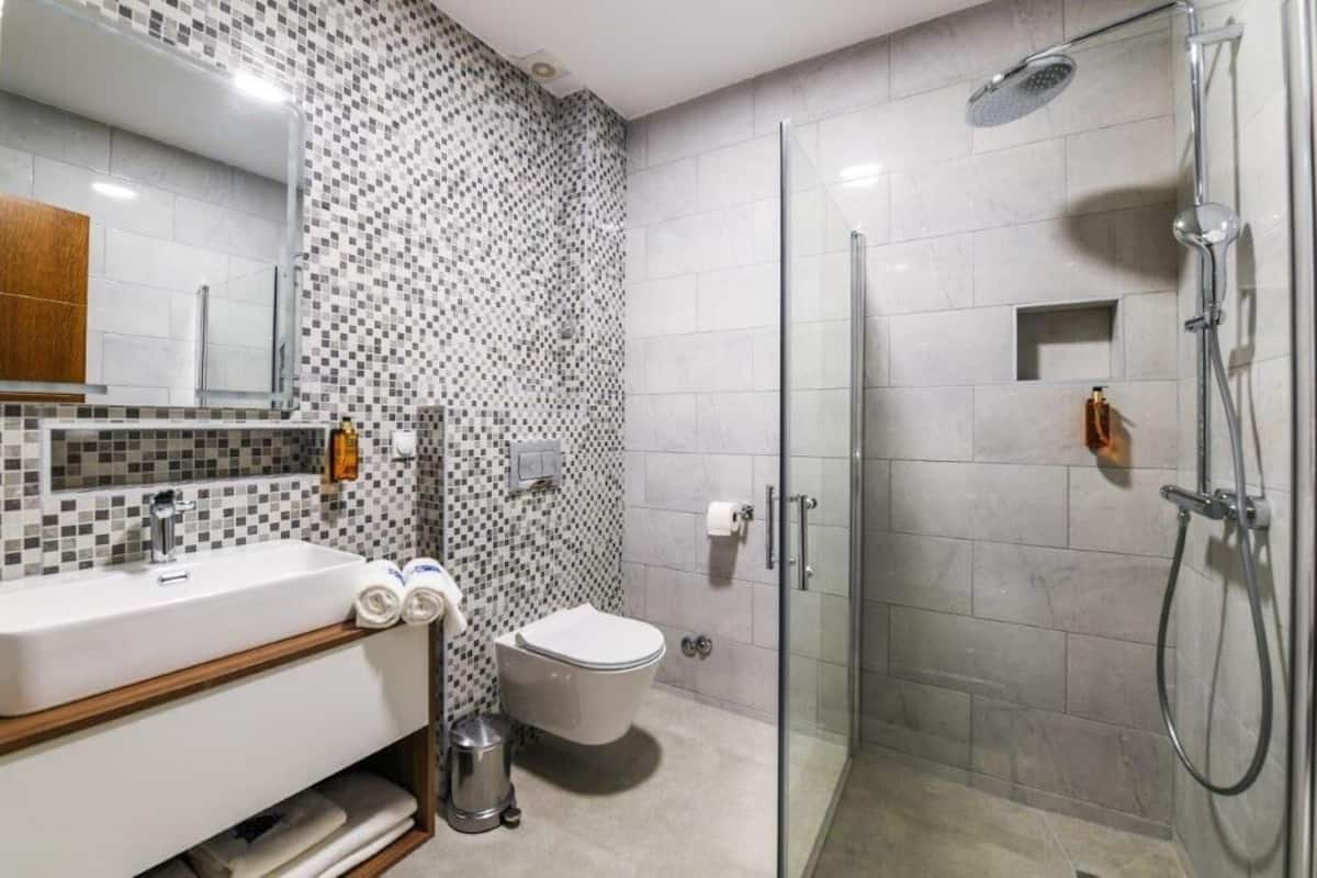 A modern bathroom with a glass-enclosed shower, a white sink with a wooden vanity, and a tiled backsplash.