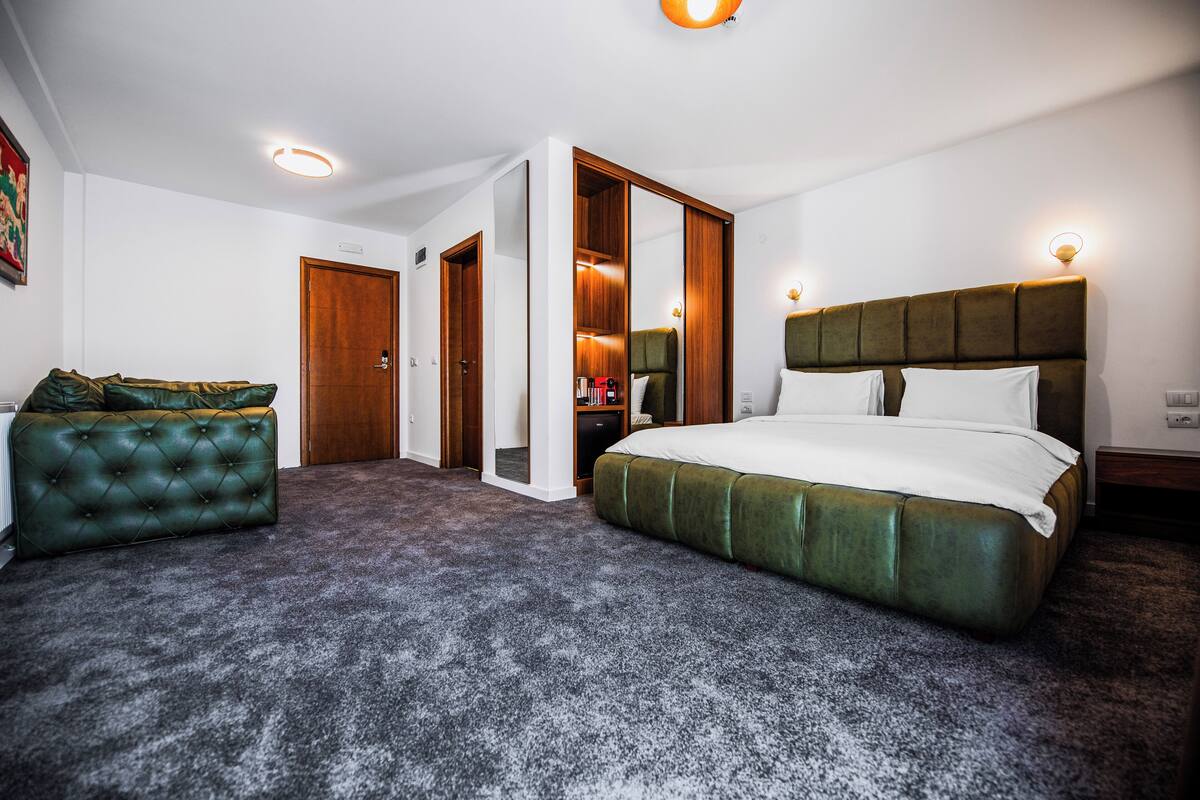 A bedroom with a large bed, a green upholstered sofa, a walk-in closet, and a wooden door.