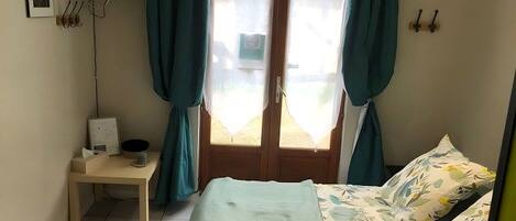 A bedroom with a bed, a desk, a chair, a TV, and a window with curtains.