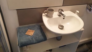 A bathroom with a white sink, a cup, and a blue towel on a shelf.