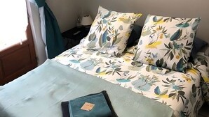 A bed with floral bedding, a teal throw blanket, and a pillow with a tag.