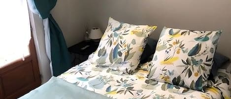 Una cama con ropa de cama estampada, un plaid color aguamarina y una almohada con una etiqueta.