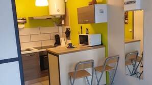 A compact kitchen with a microwave, coffee maker, and a small island with chairs.