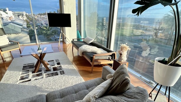 Una sala de estar moderna con un sofá grande de color gris, una mesita y un ventanal con vista a la ciudad.