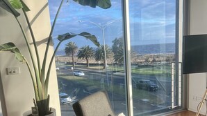 Una sala de estar moderna con un ventanal grande, una planta en maceta, un sillón cómodo y un televisor de pantalla plana.