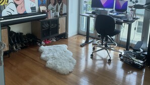 Un espacio de oficina moderno con un escritorio grande, dos monitores, una computadora portátil y un teclado. Hay un cuadro en la pared, un tapete mullido en el suelo y una ventana con vistas a edificios.