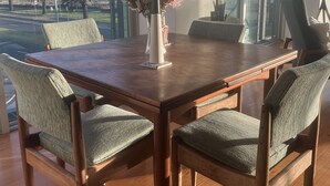 Un comedor con una mesa y sillas de madera, un jarrón con flores y vistas al océano a través de amplios ventanales.