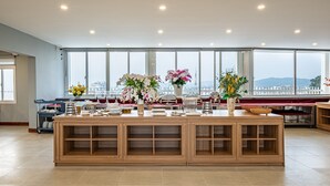 A spacious room with a large wooden buffet table, multiple flower arrangements, and a view of the city through large windows. - TAHITI CENTRAL HOTEL (Phu Quoc)