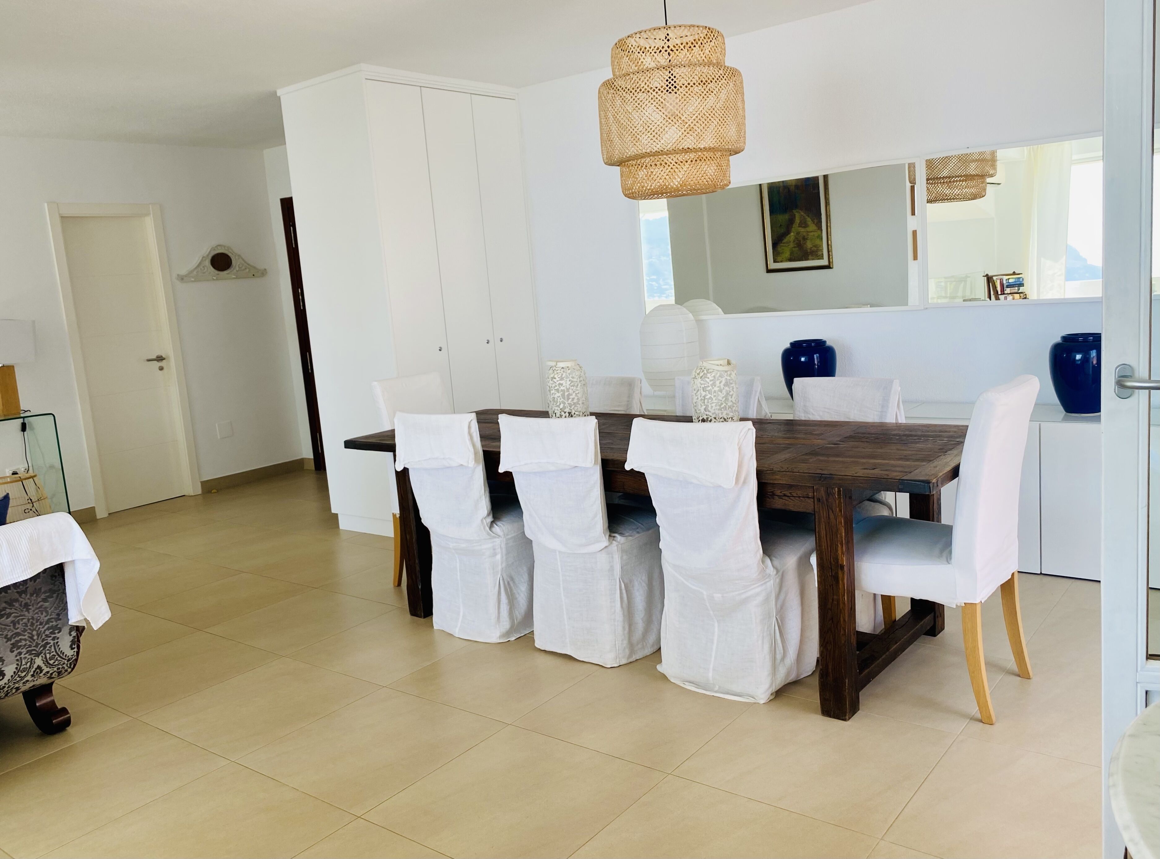 Un espace repas avec une table en bois, des chaises blanches et un luminaire suspendu.