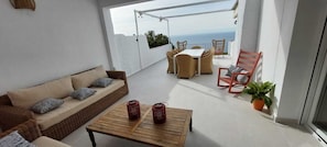 Ein Balkon mit einer Couch, Korbstühlen, einem Tisch und Blick aufs Meer.