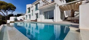 Ein moderner Poolbereich mit klarem Pool, weißen Wänden und einem Balkon mit Korbmöbeln.