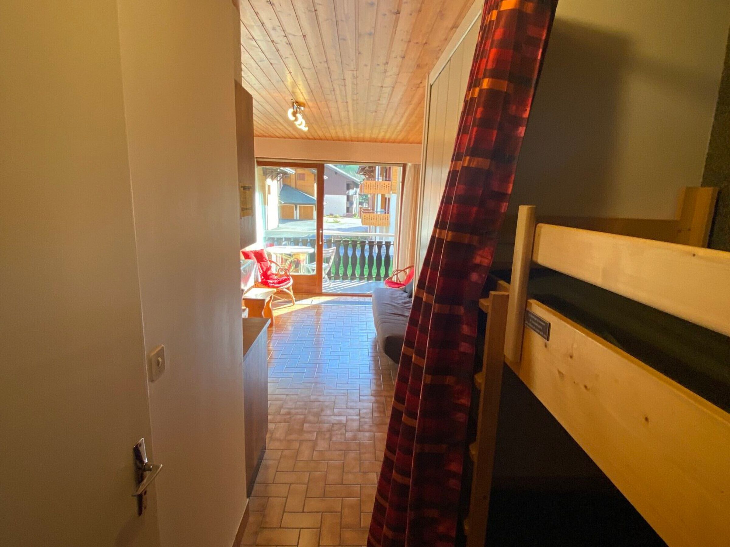 Ein Korridor, der zu einem Balkon mit Holzboden, einem roten Karomuster-Vorhang und einer Bank führt.