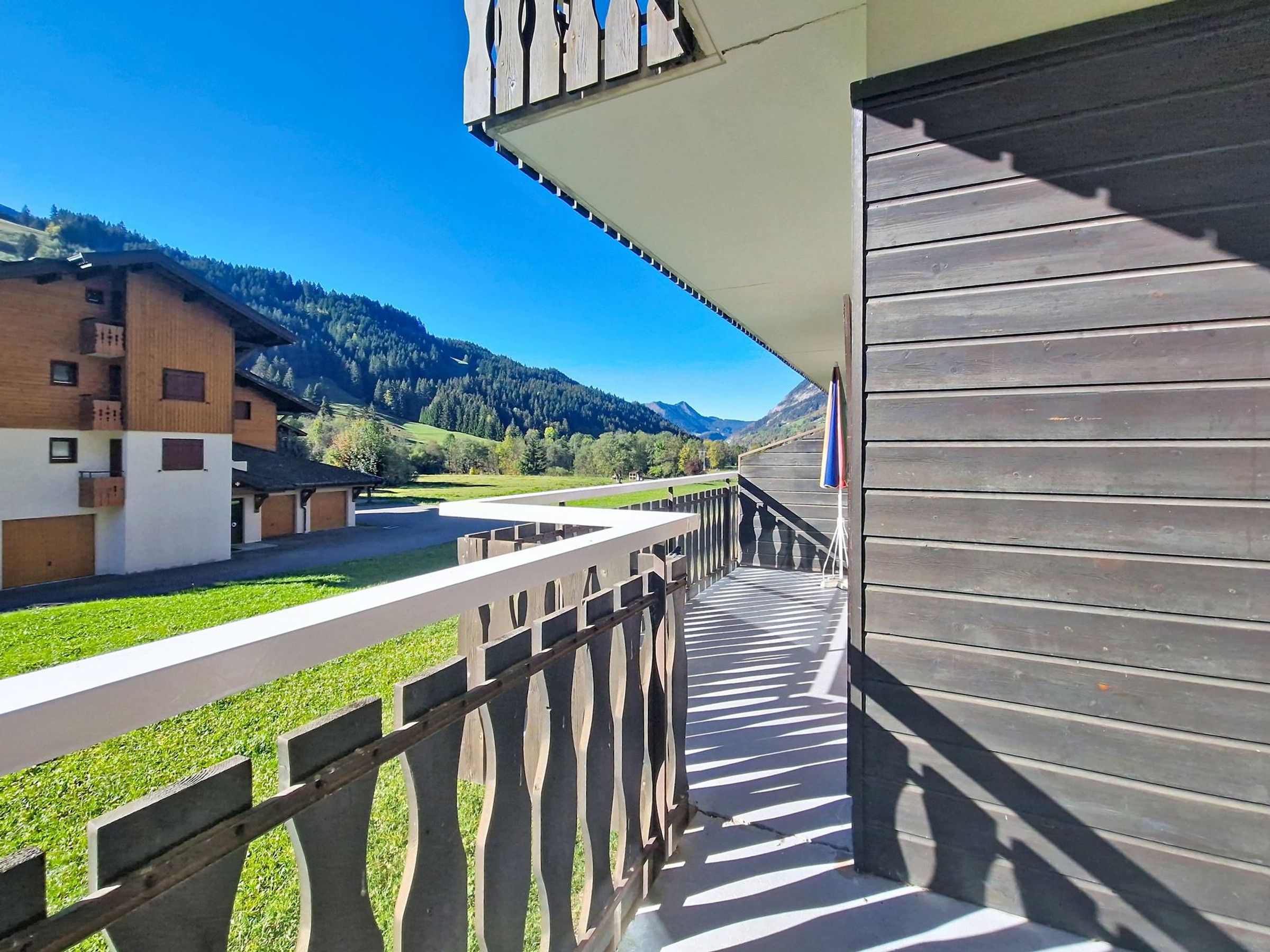 Un balcon donnant sur un paysage montagneux, une clôture en bois et un bâtiment doté d’un toit en pente.