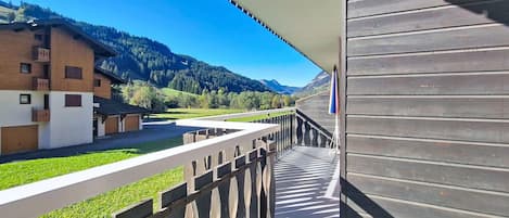 Un balcon donnant sur un paysage montagneux, une clôture en bois et un bâtiment doté d’un toit en pente.