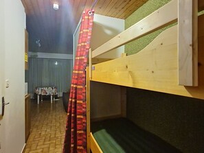 Une chambre avec des lits superposés, un plafond en bois, un rideau à motifs et une table avec des chaises à l’arrière-plan.