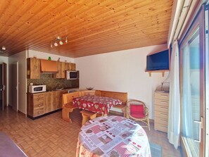 A compact room with a kitchenette, a bed with a patterned bedspread, a small table, and a chair.