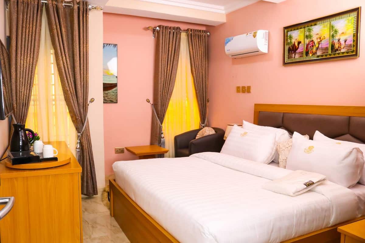 Habitación de hotel con cama, cortinas, escritorio con cafetera, silla y aire acondicionado de pared.