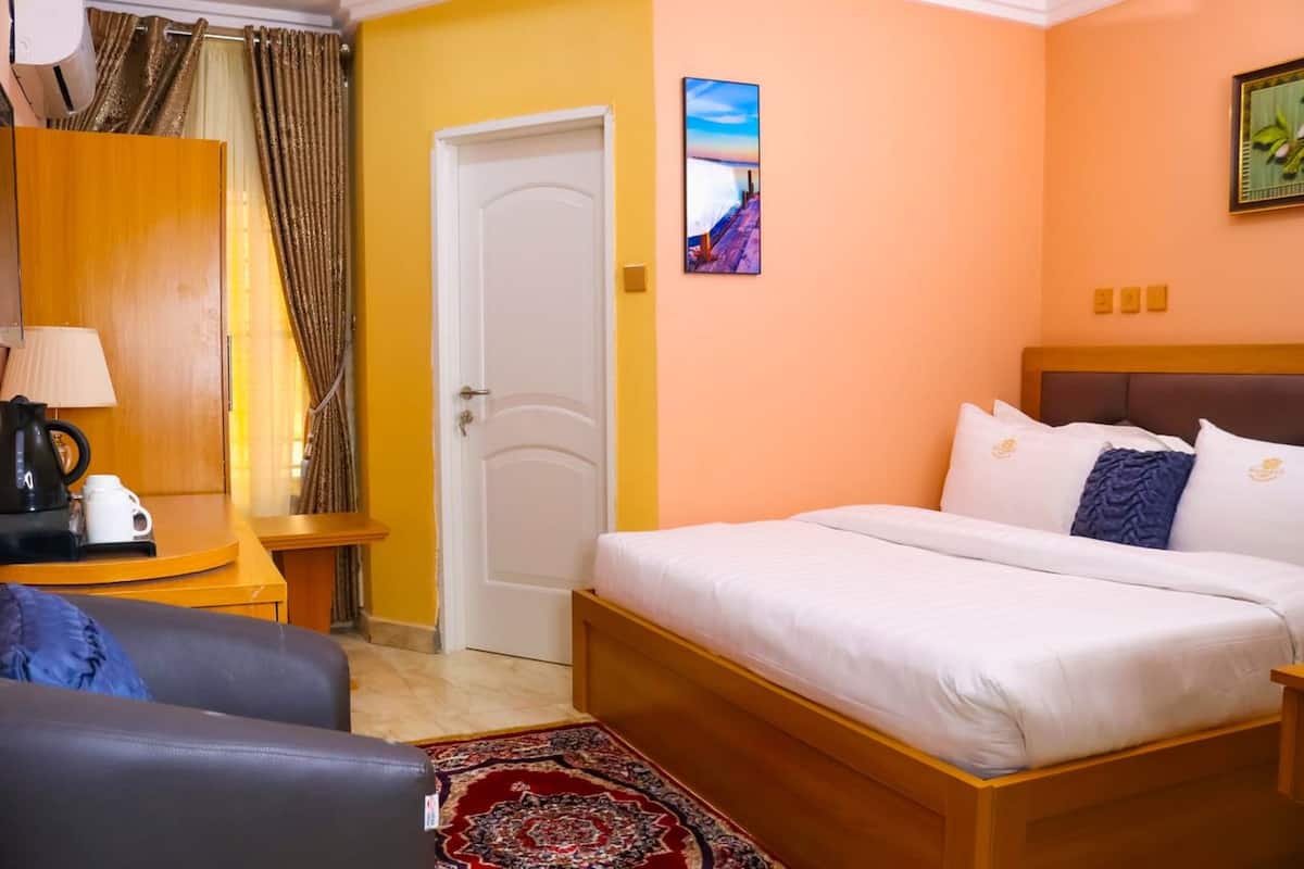 Habitación de hotel con cama, escritorio con lámpara, cafetera y vista a la calle a través del ventanal.