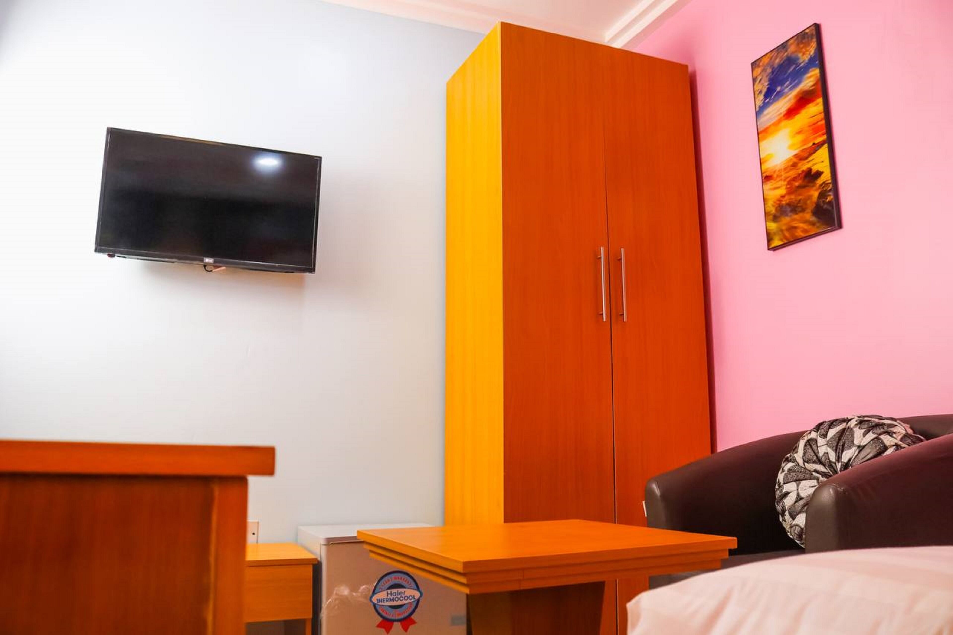 Une pièce comprenant un lit, une armoire en bois, un téléviseur fixé au mur et un tableau accroché au mur.