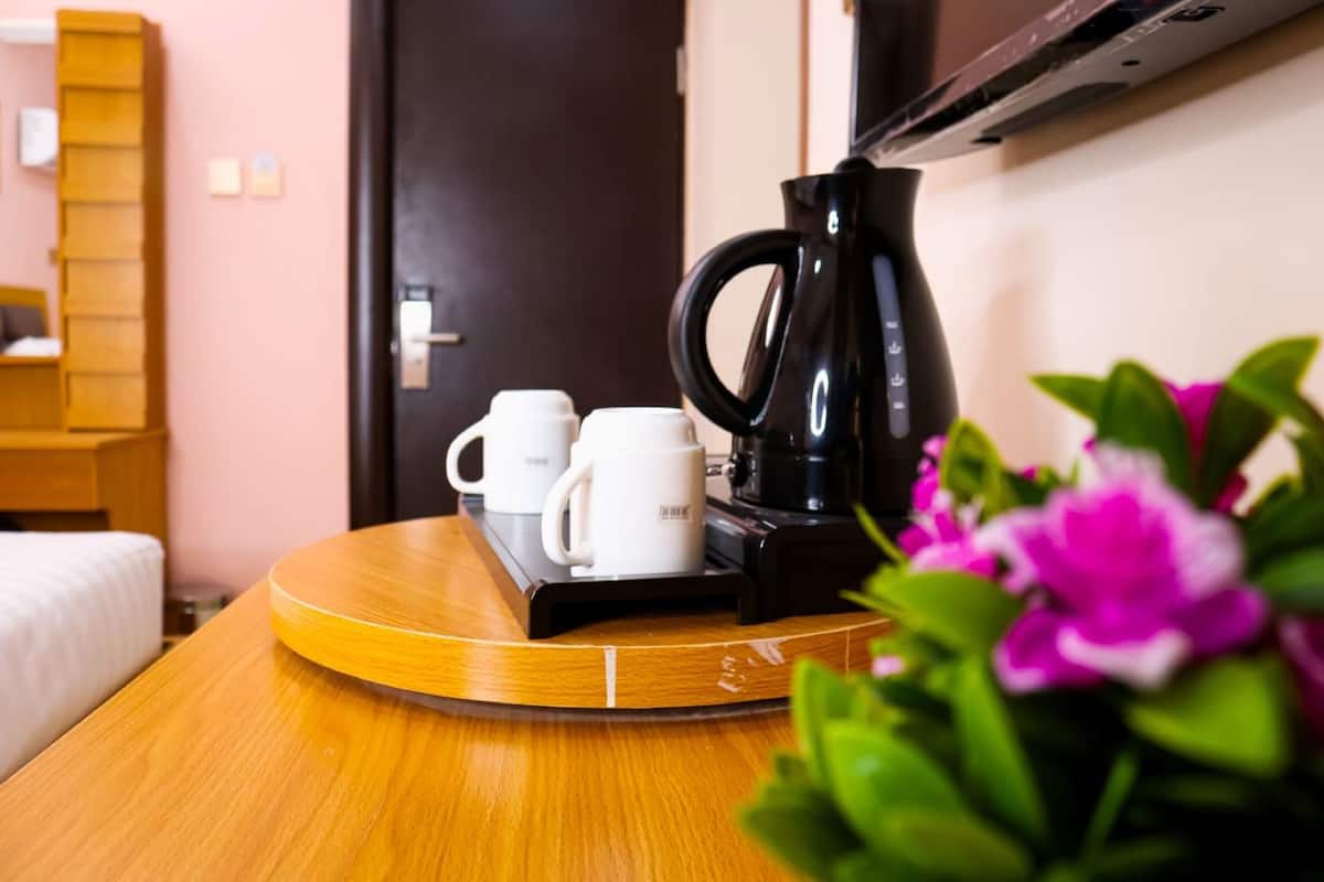 Una habitación de hotel con una mesa de madera, una cafetera negra, dos tazas blancas y una bandeja.