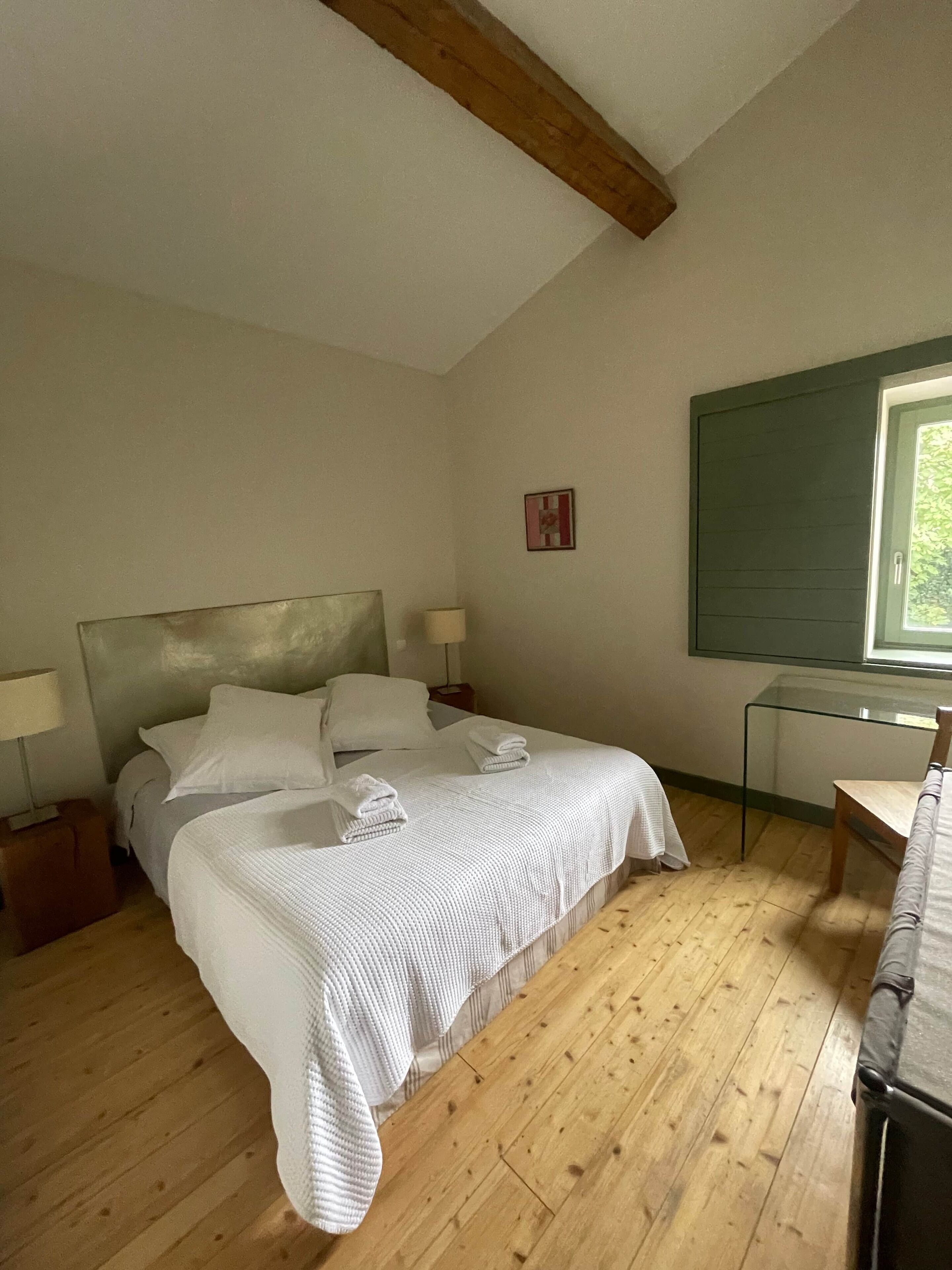 A bedroom with a bed, bedside tables, a desk, and a window.