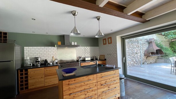 A modern kitchen with wooden cabinetry, a central island, and a stone exterior wall. - Luxury House - Exceptional (Roquefort-des-Corbières)