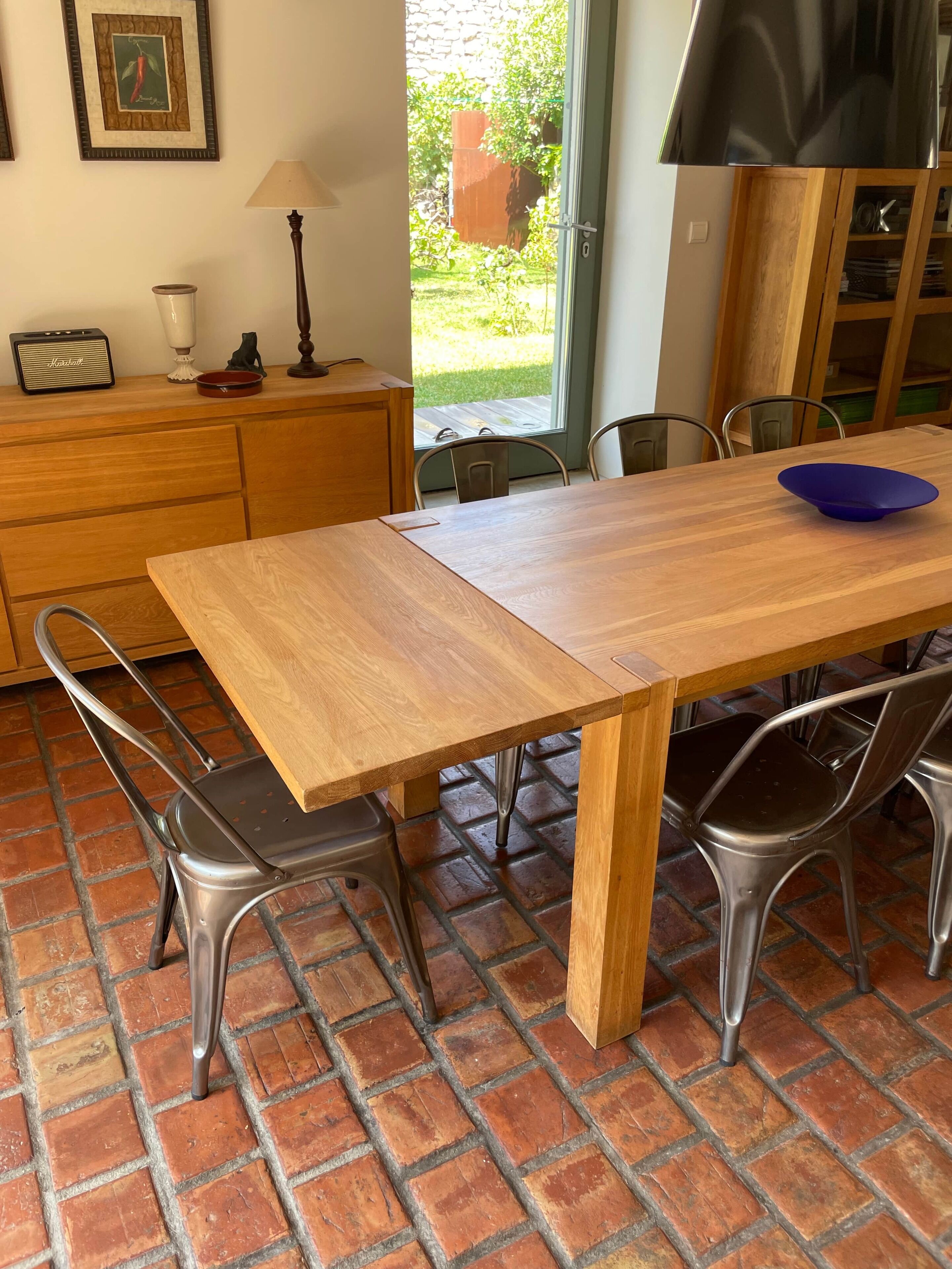 A dining area with a wooden table, metal chairs, a blue bowl, a lamp, and a vintage radio.