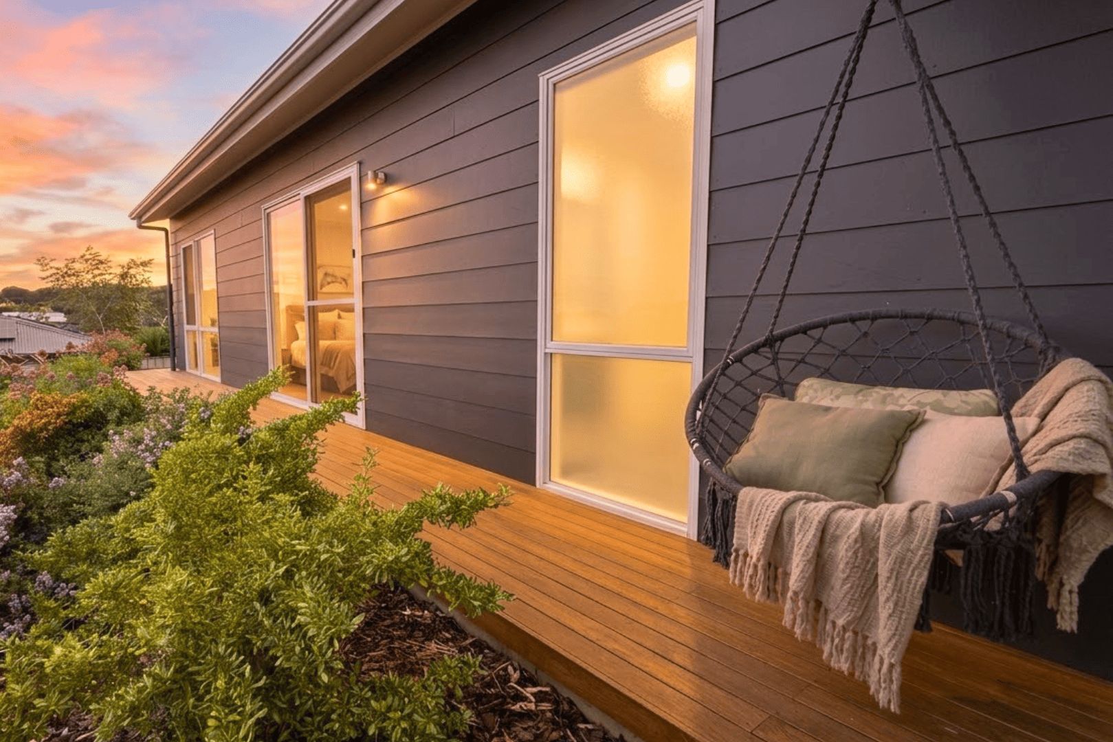 A modern house with a wooden deck, a hanging chair, and a glass door leading to a bedroom.