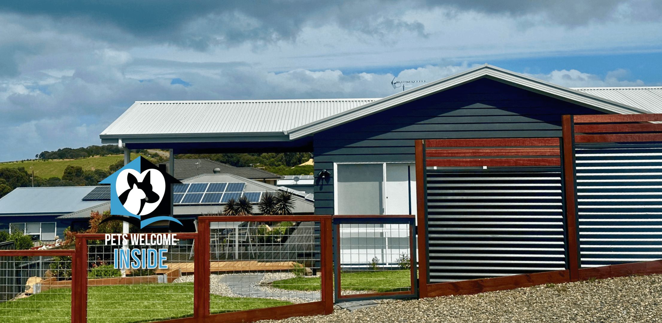 Een modern gebouw met een dak van zonnepanelen, een omheind gebied en een bord waarop staat: 'HUISDIEREN WELKOM'.