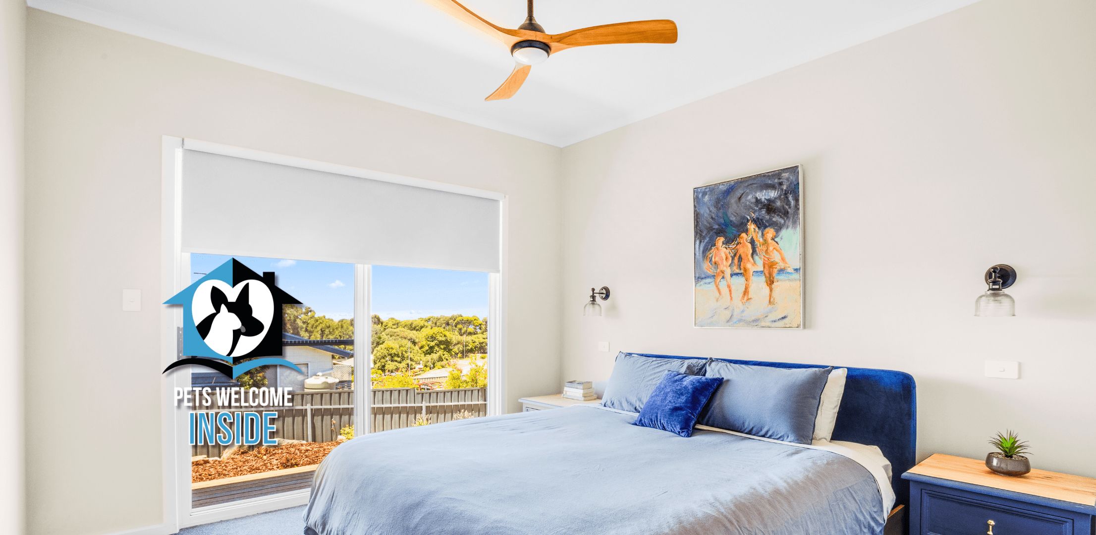 A bedroom with a bed, a ceiling fan, a painting, and a view of the outdoors.