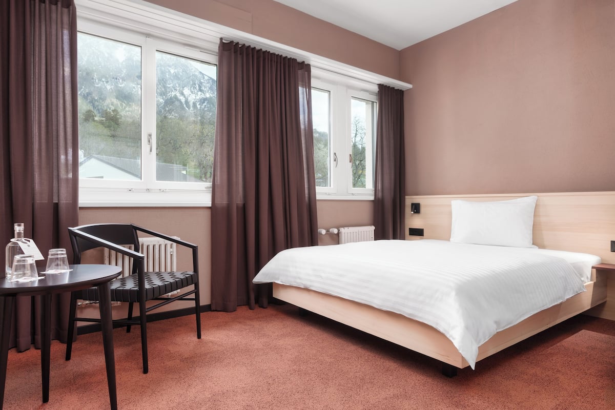 A hotel room with a bed, a chair, a table, and a window with curtains.