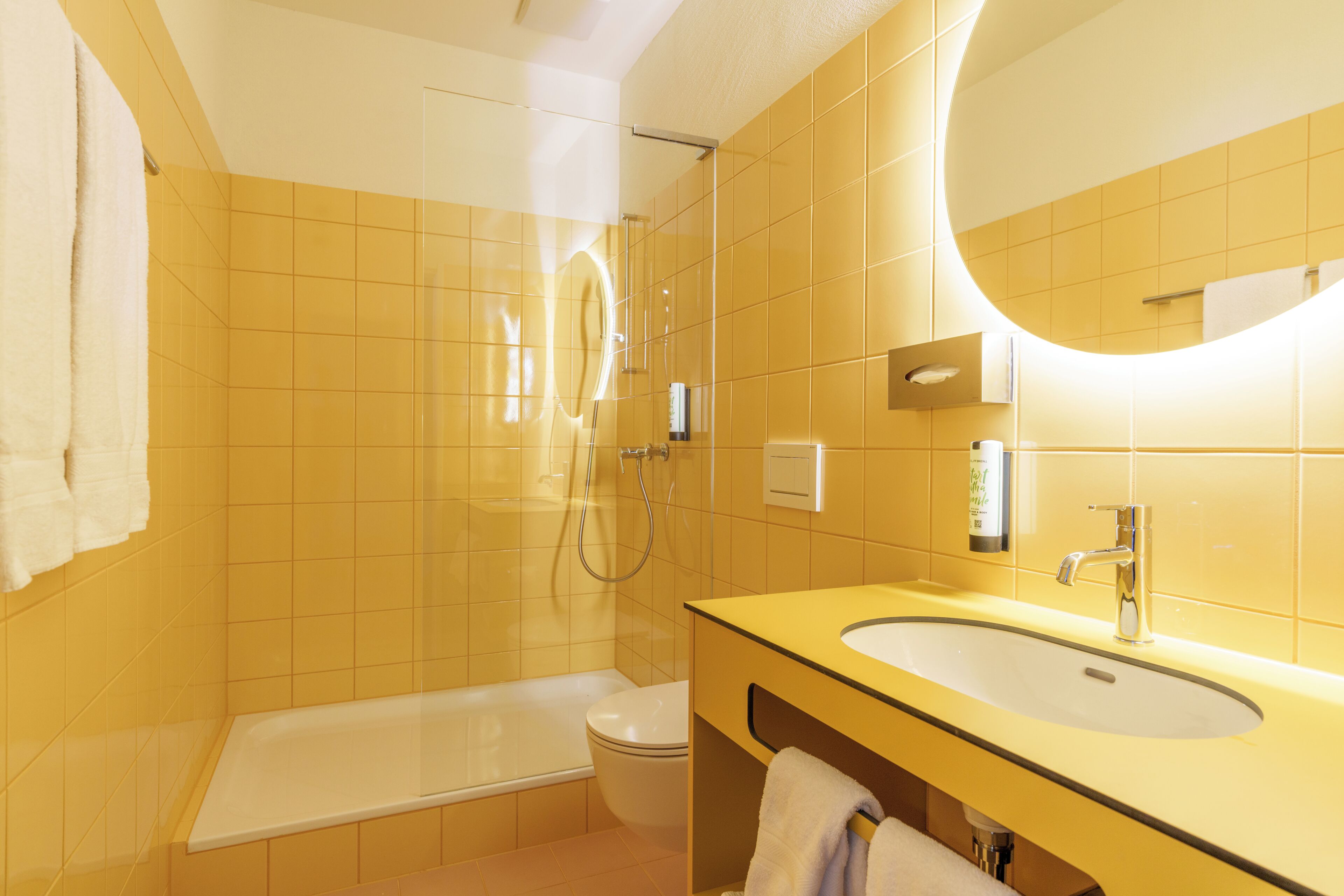 A bathroom with yellow tiles, a bathtub, a toilet, a sink, and a mirror.