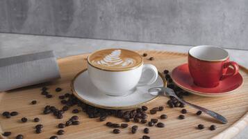 Een witte kop met latte-art op een houten dienblad, een rode kop op een schotel, en losse koffiebonen.