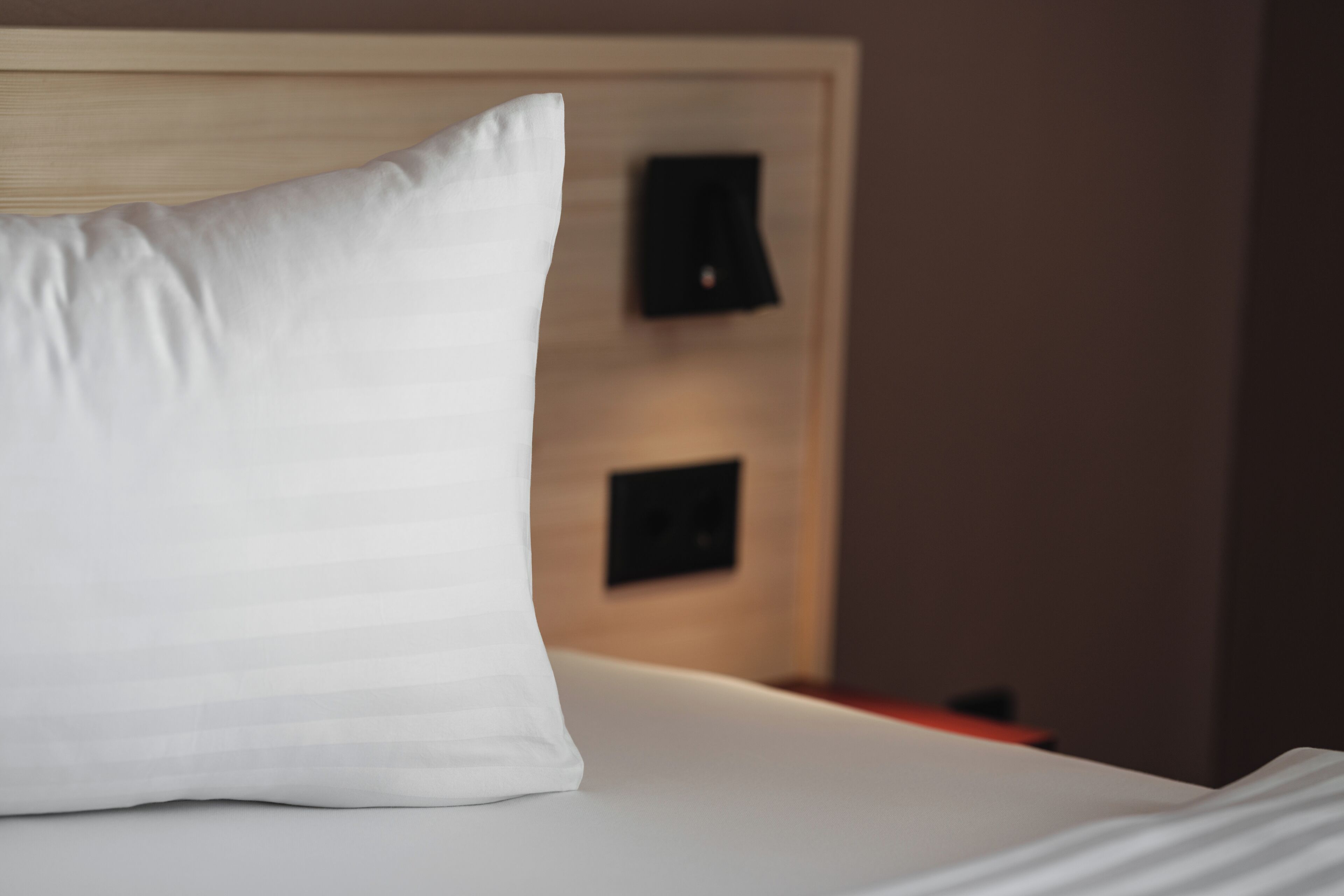A neatly made bed with a white pillow and a wooden headboard.
