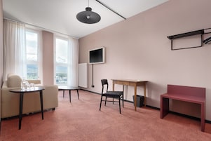 Habitación de hotel con sofá, una mesita, una silla, un escritorio, un televisor y una ventana con vistas.