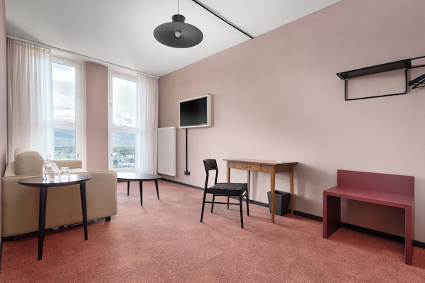 Habitación de hotel con sofá, una mesita, una silla, un escritorio, un televisor y una ventana con vistas.