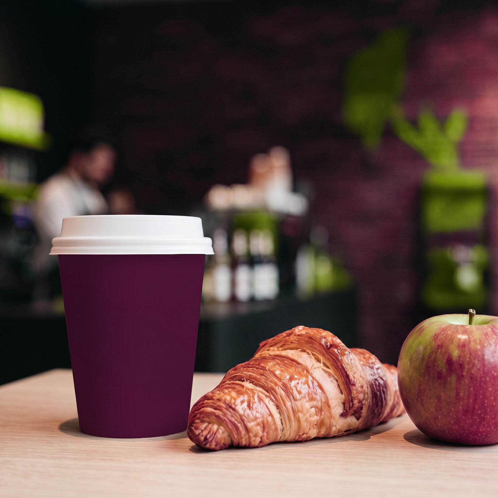 Ein Croissant, ein Apfel und eine Kaffeetasse auf einem Tisch.