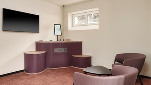 A modern room with a flat-screen TV, a small table, two chairs, a purple console, and a window with a view. - Kloster by bsmart (Schaan)