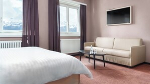 A hotel room with a bed, a sofa, a coffee table, a TV, and a window with curtains. - Kloster by bsmart (Schaan)