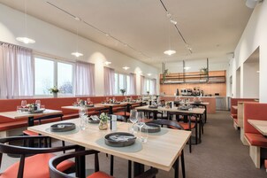 Un comedor amplio con varias mesas y cabinas, una cocina al fondo y grandes ventanales con cortinas.