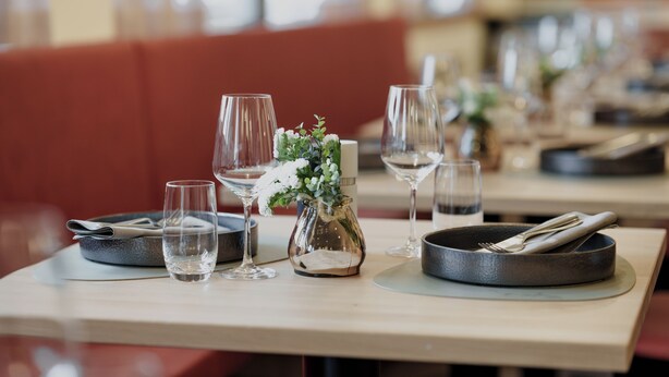 A restaurant table set with wine glasses, a vase with flowers, and cutlery. - Kloster by bsmart (Schaan)