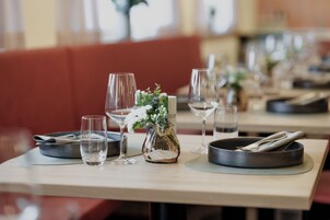 Una mesa de restaurante dispuesta con copas de vino, un jarrón con flores y cubiertos.