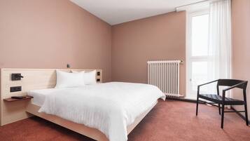 A bedroom with a bed, a chair, a nightstand, a radiator, and a window with curtains.