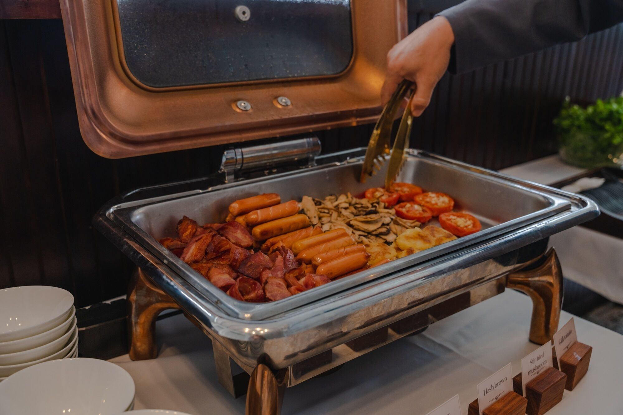 Un bufé con varios perros calientes, tocino, champiñones y tomates.