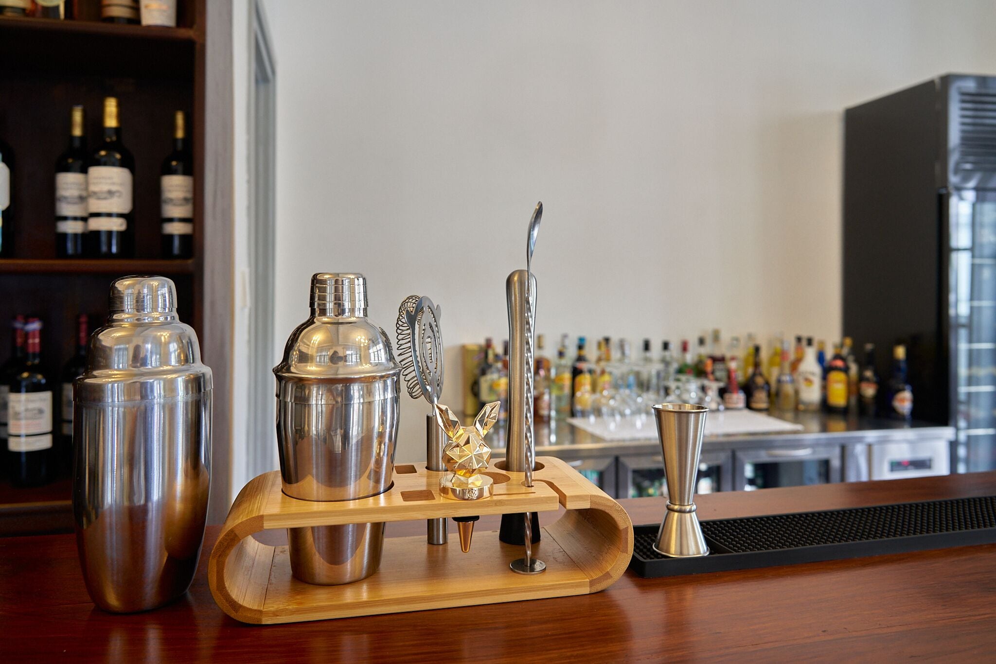 A bar area with a wooden bar counter, a cocktail shaker, a bottle of liquor, and a bottle of wine.