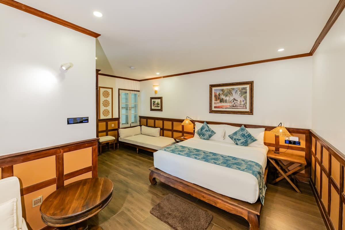 Een hotelkamer met een groot bed, een houten bankje, een kleine tafel en een tv aan de muur.