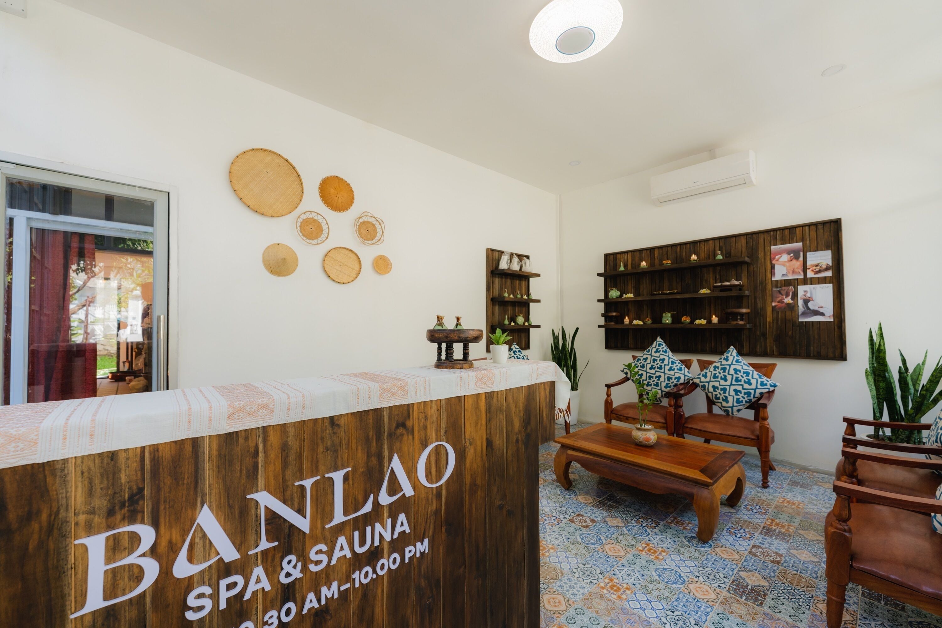 A reception area with a wooden counter labeled "BANLAO SPA & SAUNA," a tiled floor, wooden furniture, and wall decorations.